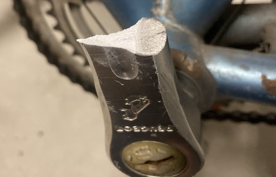 Broken bicycle pedal with Peugeot logo upside down. Bike frame in the background. Close up of crack