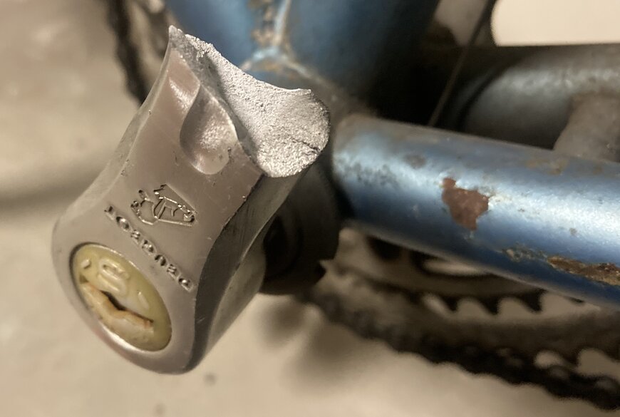 Broken bicycle pedal with Peugeot logo upside down. Bike frame in the background. Close up of crack