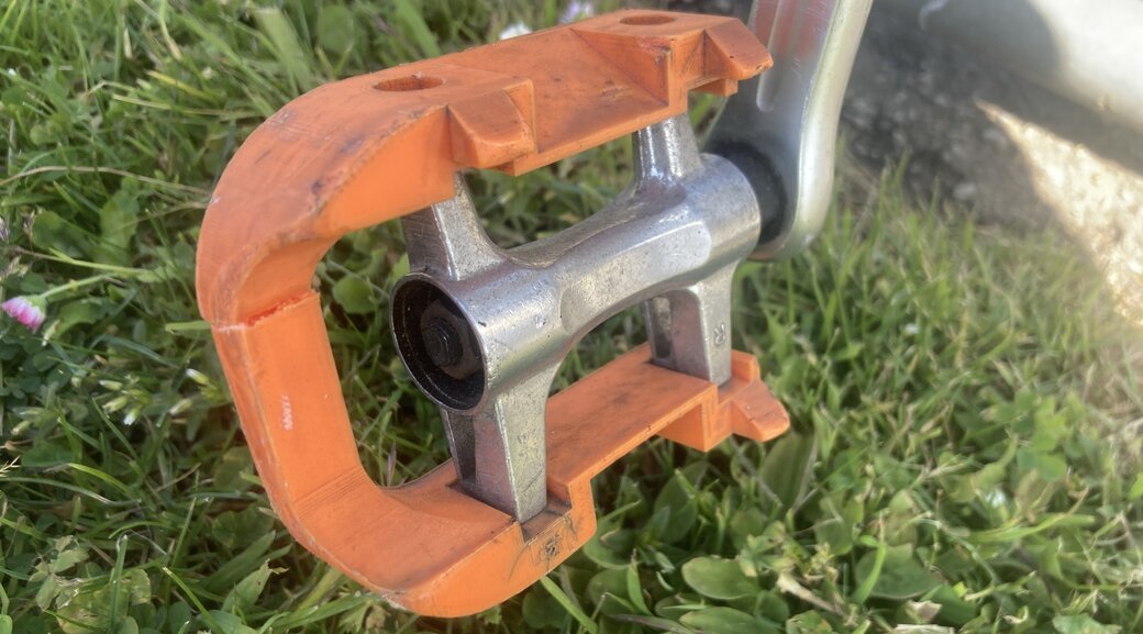 Bike pedal made of orange plastic, broken. Side view