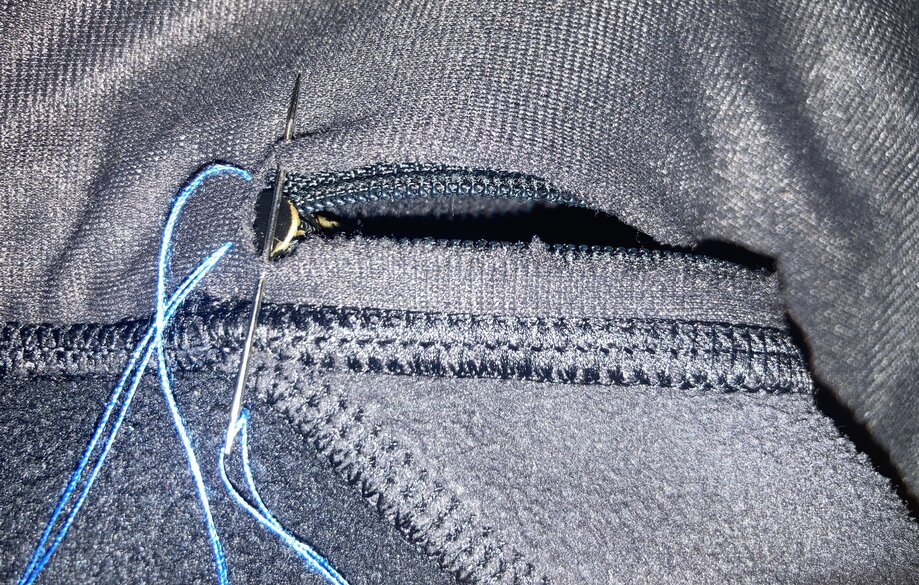 Long curved hole in black fabric. Needle with blue thread inserted near the hole