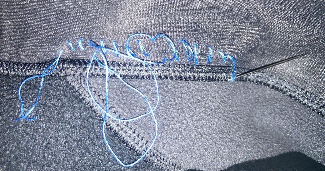Black fabric with blue thread haphazardly tangled around a seam where the hole used to be
