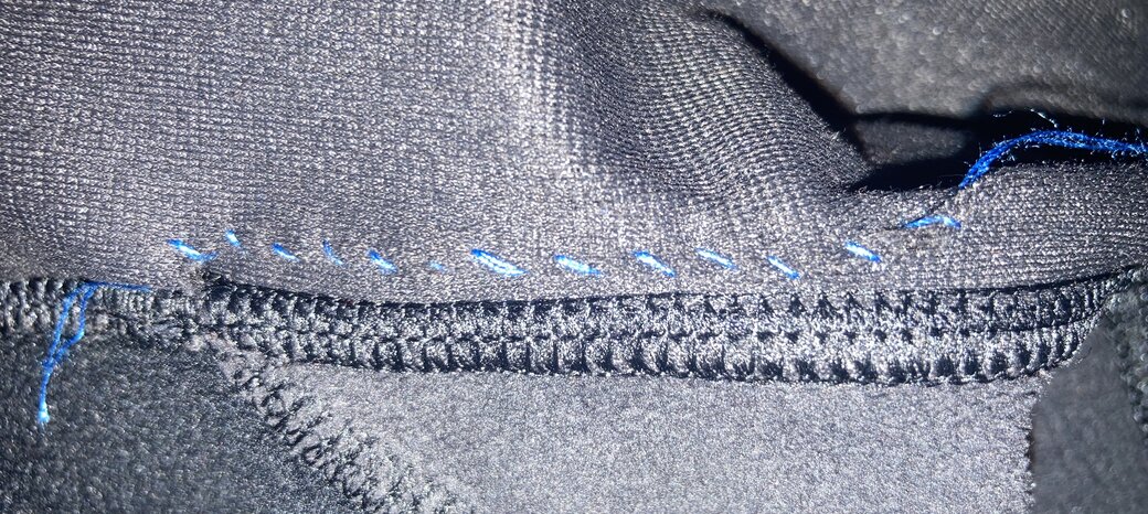 Black fabric with neat blue thread pulled taught at regular intervals to close the hole